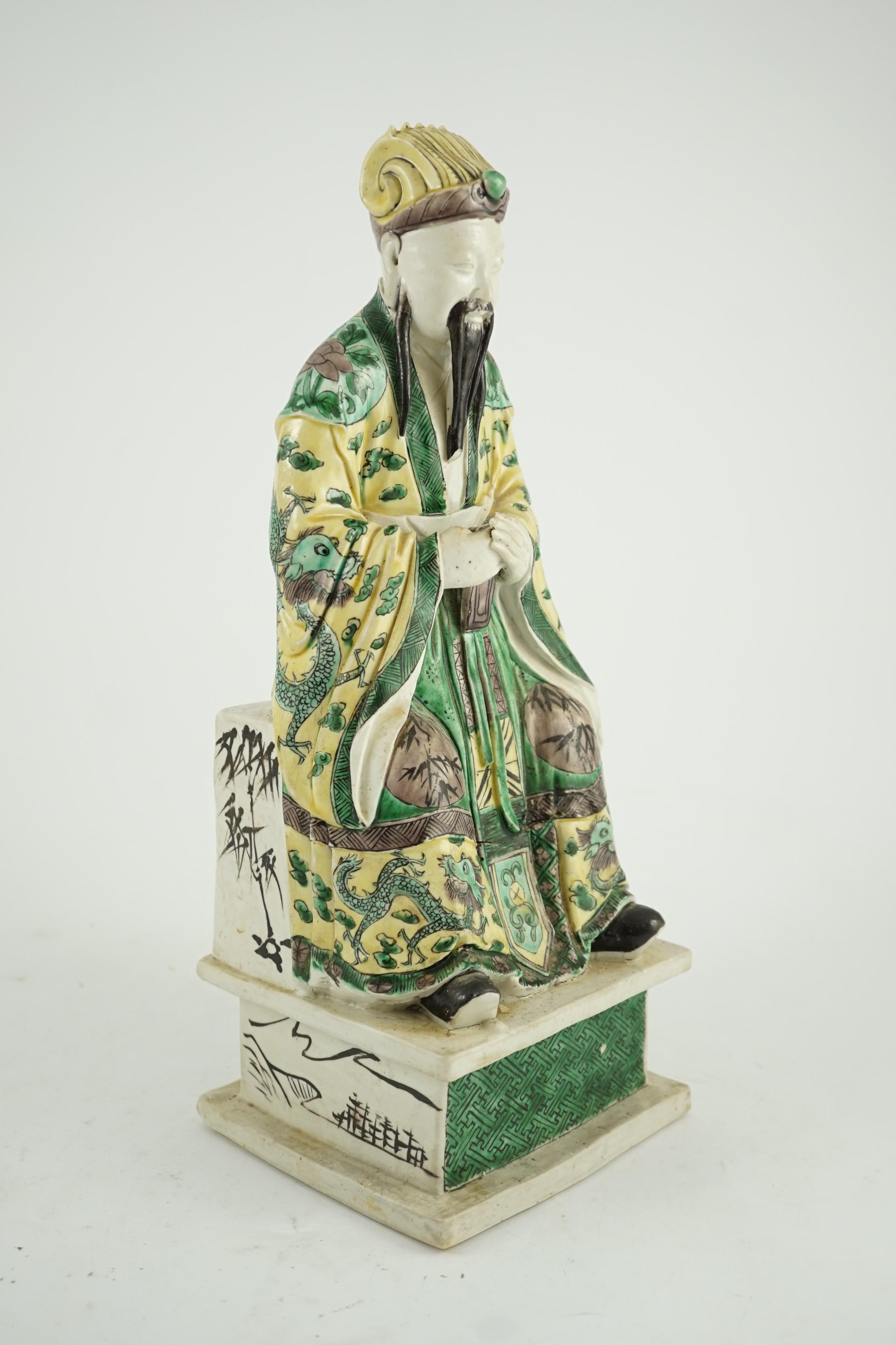 A Chinese enamelled biscuit figure of a seated court official, Kangxi period, 31.5cm high, small losses